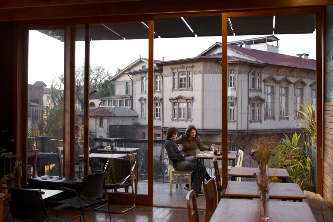Two people dining on a modern terrace with Victorian mansions visible through large glass doors in Valparaíso.