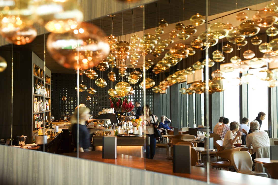 Modern restaurant interior with hanging golden pendant lights and diners at tables.