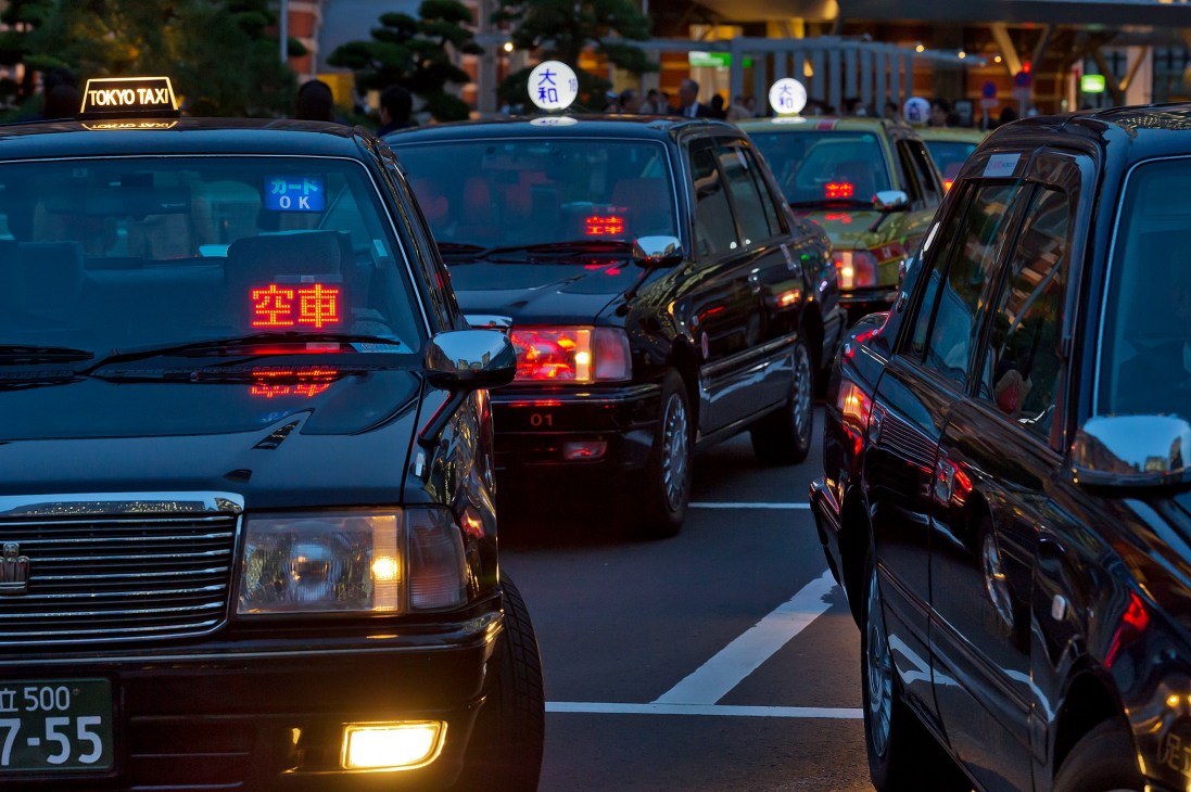 Tokyo taxis lined up at night with illuminated dashboard lights and rooftop signs displaying 'Available' status.