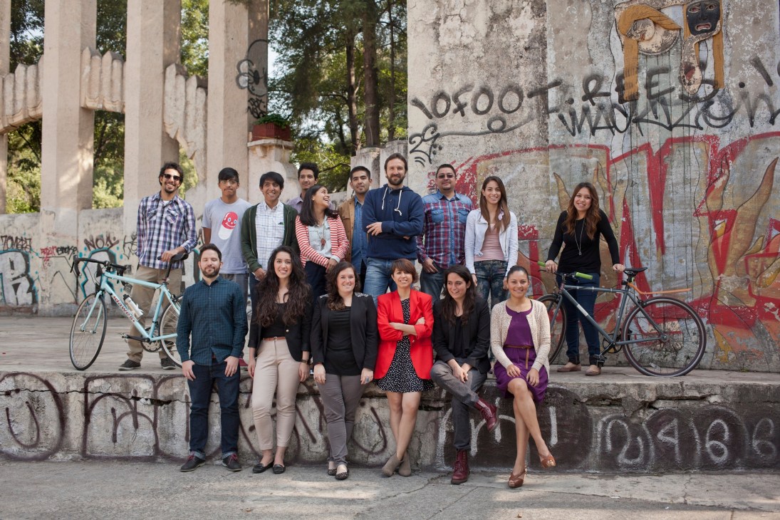 Group portrait of the Laboratorio para la Ciudad team posing in front of a graffiti-covered concrete wall with bicycles.