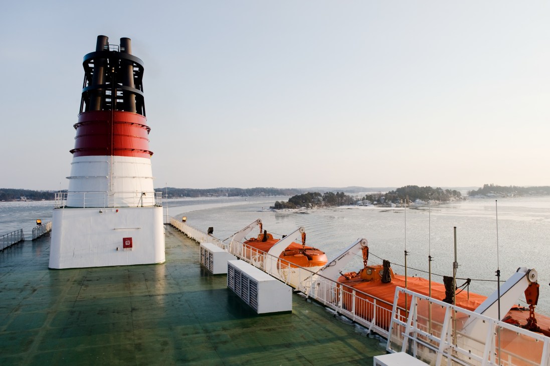 A red and white lighthouse with black lantern room structure stands in shallow water near Stockholm archipelago islands.