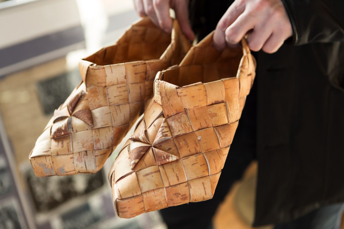 Hands holding two traditional Finnish birch-bark shoes with woven construction.