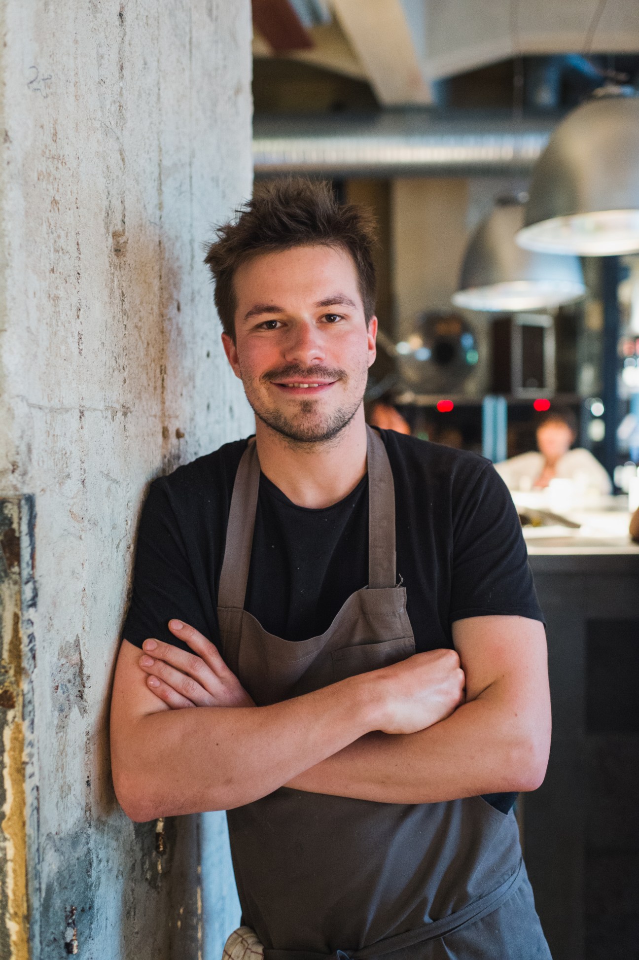 Chef in brown apron leaning against white wall in restaurant kitchen at BasBas, Helsinki
