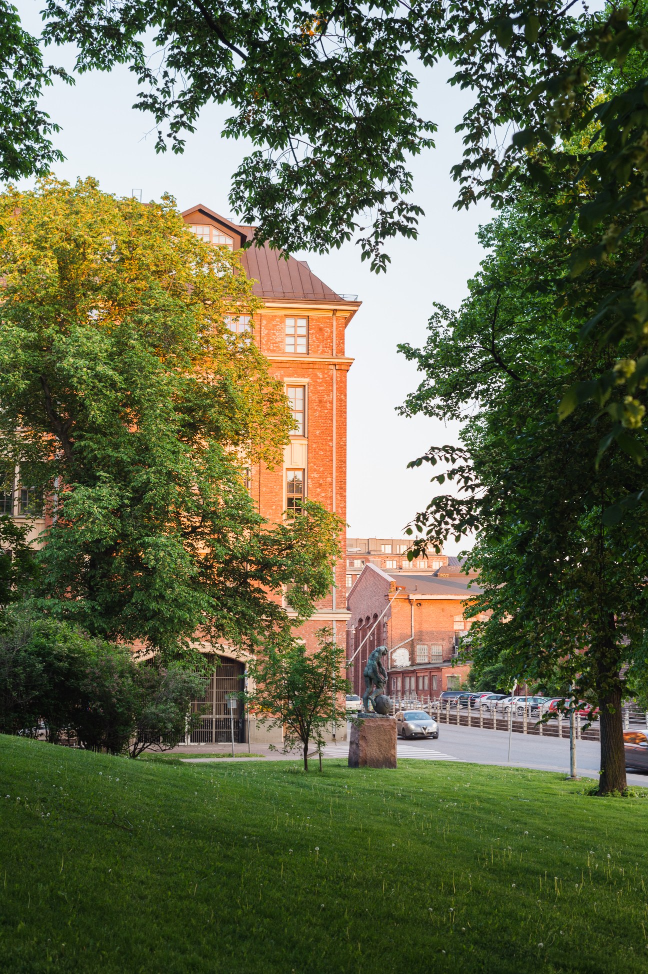 Telakkapuistikko Park in Helsinki with red brick buildings framed by lush green trees and manicured lawn.
