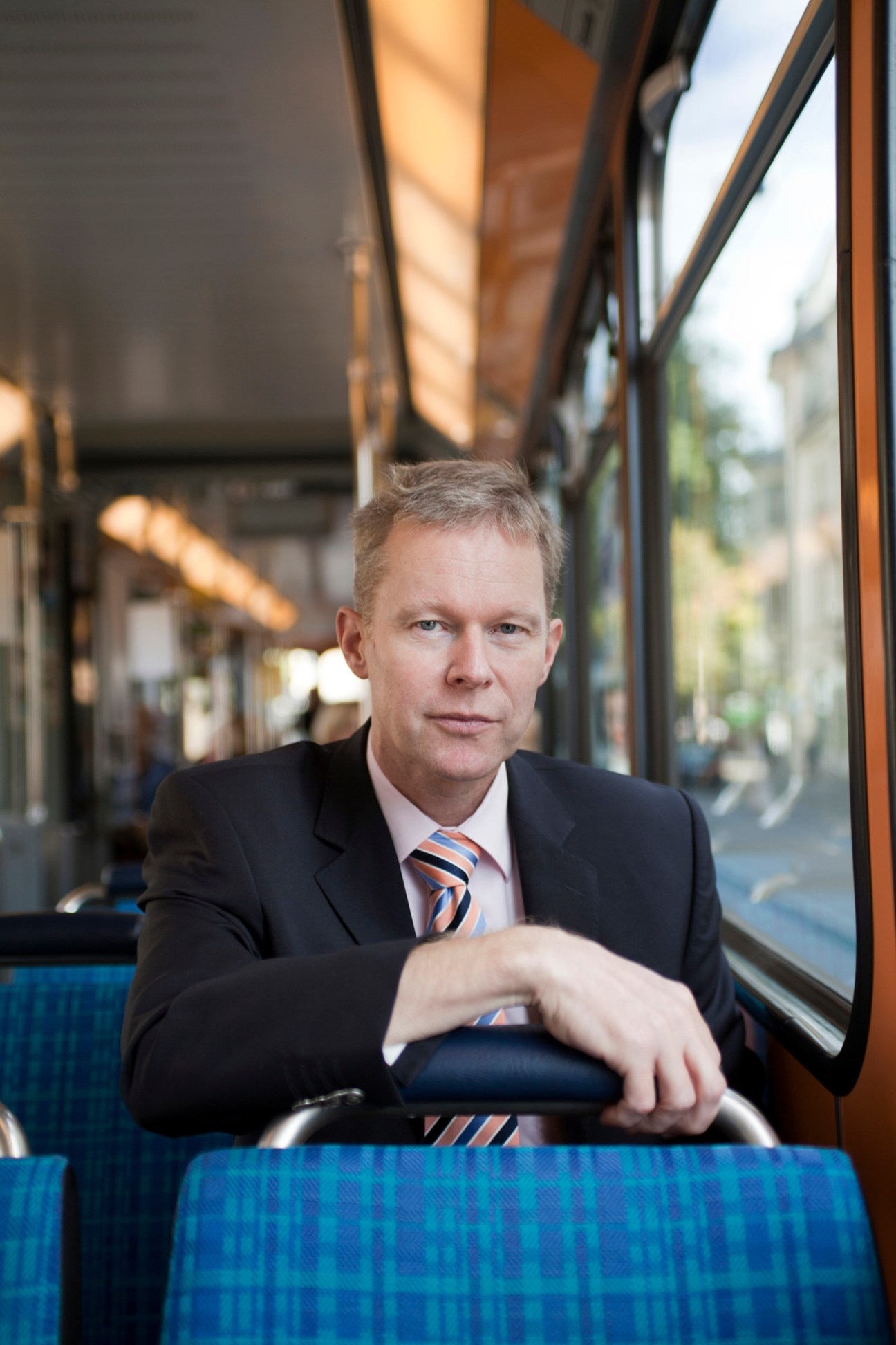 Andreas Uhl, head of corporate staff at VBZ Zurich public transport, seated on a tram wearing a dark suit and striped tie.