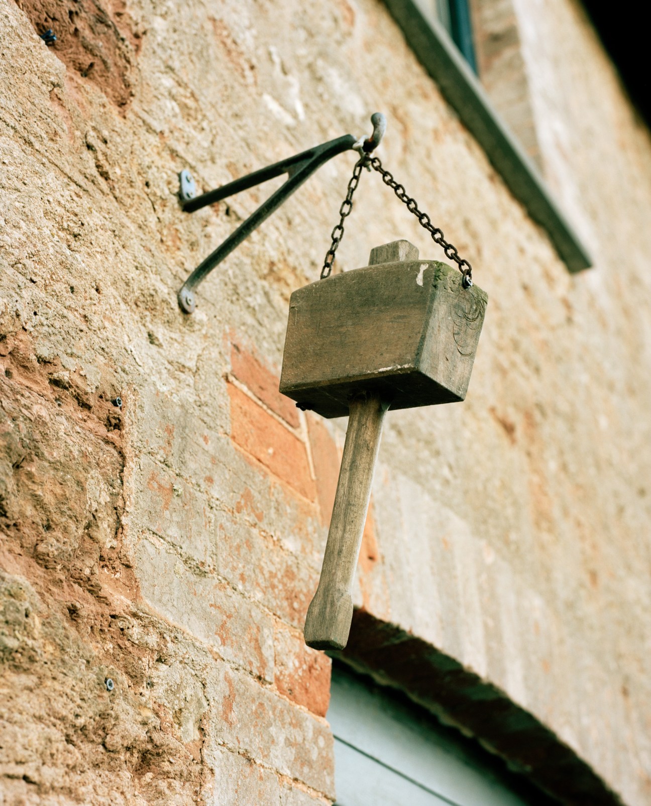 Wooden birdhouse with metal chain hanging from a weathered brick wall.