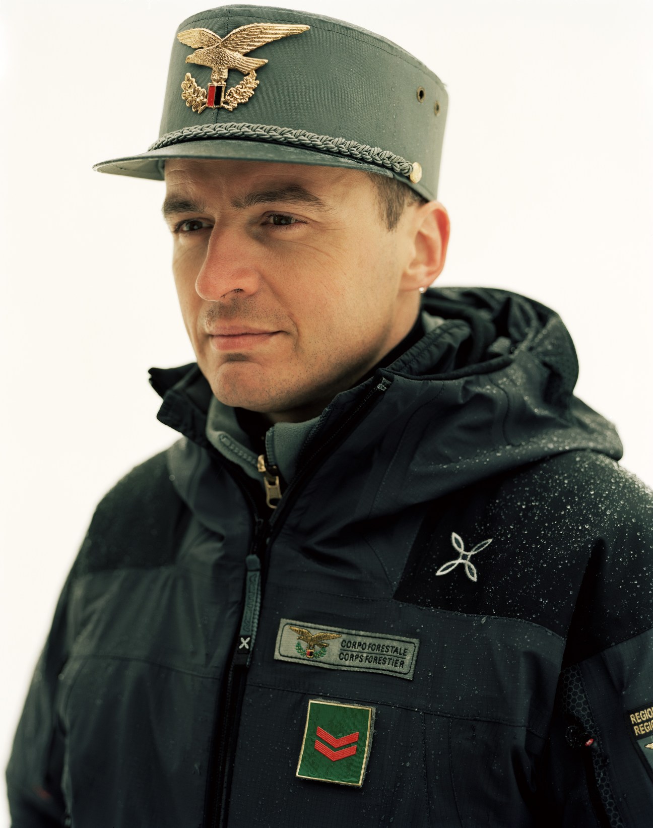 Italian forest ranger in uniform with green military cap and jacket against white background.