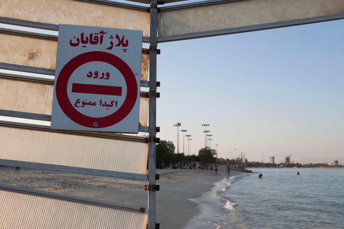 No entry sign in Persian on a men-only beach in Kish with swimmers in the Persian Gulf beyond.