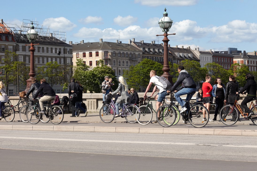People cycling and walking near ornate street lamps with Copenhagen buildings in the background.