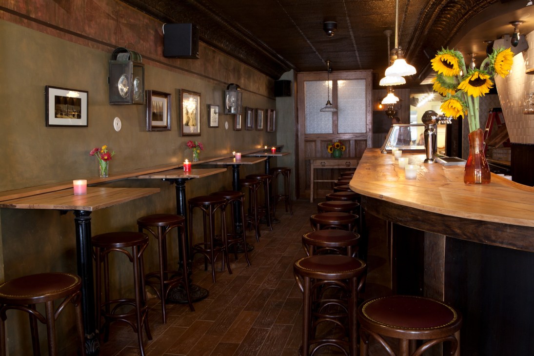 Interior of Rubirosa restaurant in New York with wooden tables, dark chairs, and sunflower arrangements.