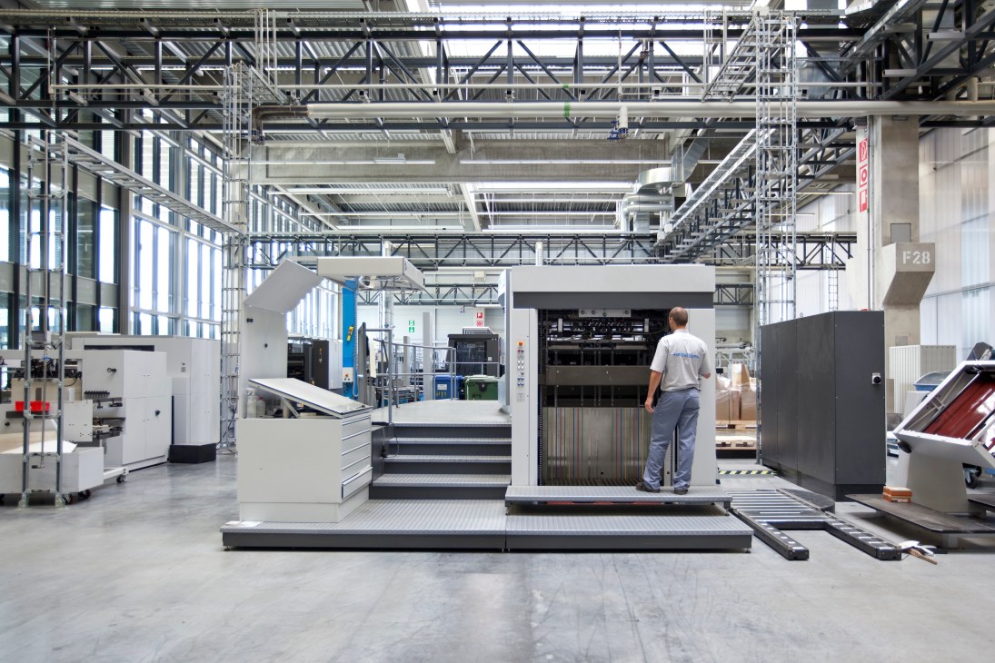 Worker operating a large Heidelberg printing press in a factory production room