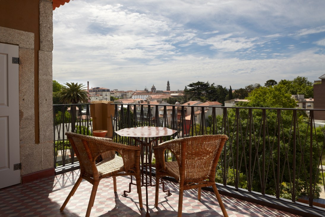 Balcony terrace with wicker chairs overlooking Porto's historic centre cityscape.