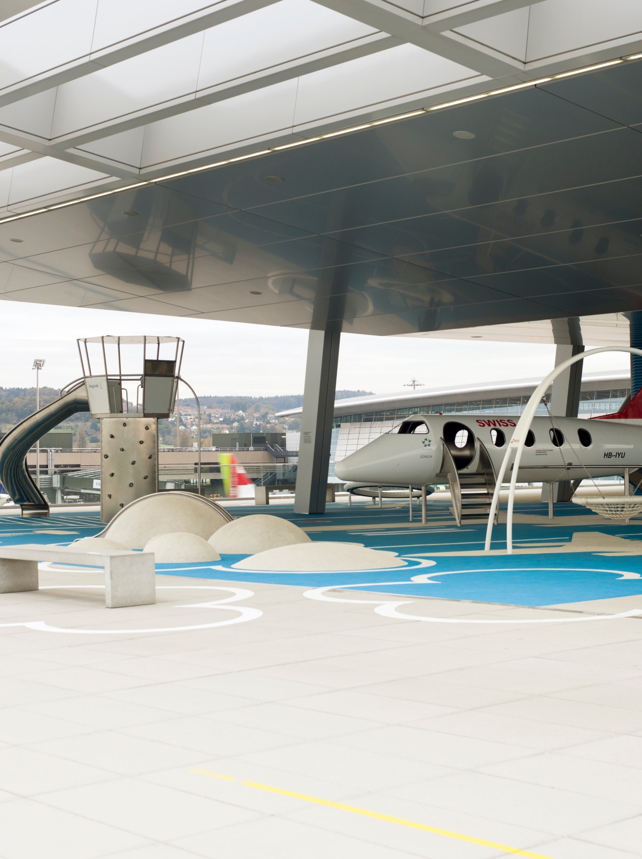 Modern airport terminal interior with blue flooring, white aircraft model, and architectural elements under skylight.