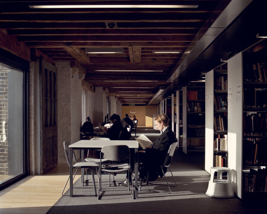 Students studying at tables in a modern library with exposed wooden beams and concrete pillars.