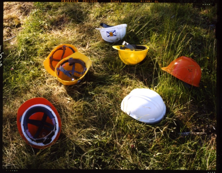 Colorful hard hats scattered on grass at a construction site.