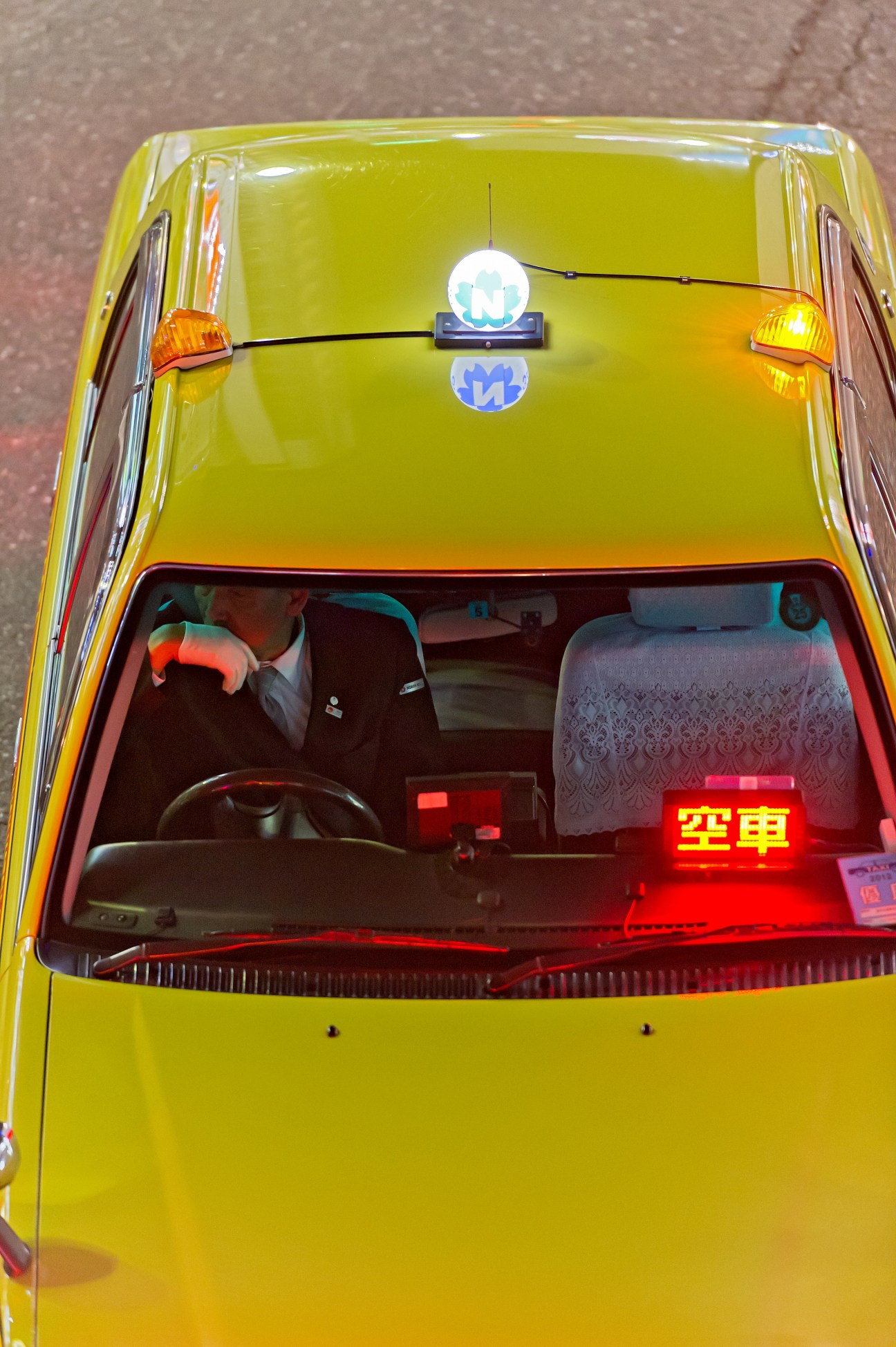 Overhead view of a yellow Tokyo taxi with red interior showing empty seats and an illuminated available light.