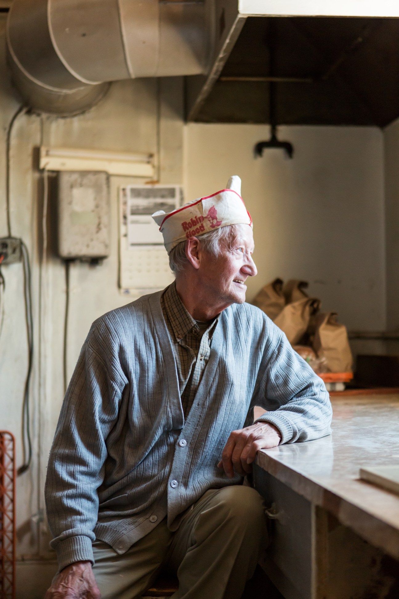 Michael Setala, an elderly Finnish-Canadian baker, sits in his bakery wearing a paper baker's hat.