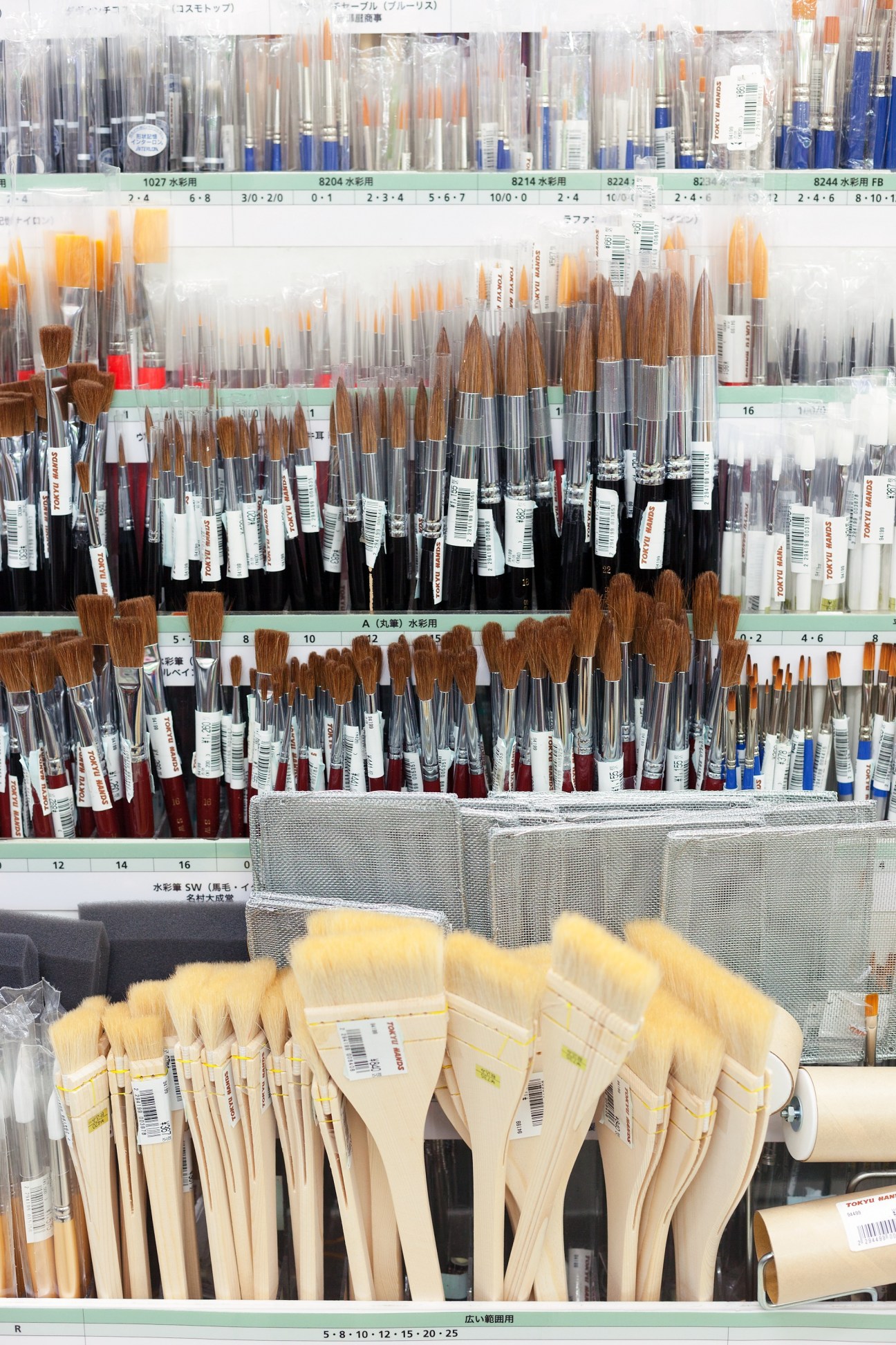 Organized display of paintbrushes with various sizes and colors arranged on shelves with Japanese labels in Tokyu Hands' Crafts & Design section.