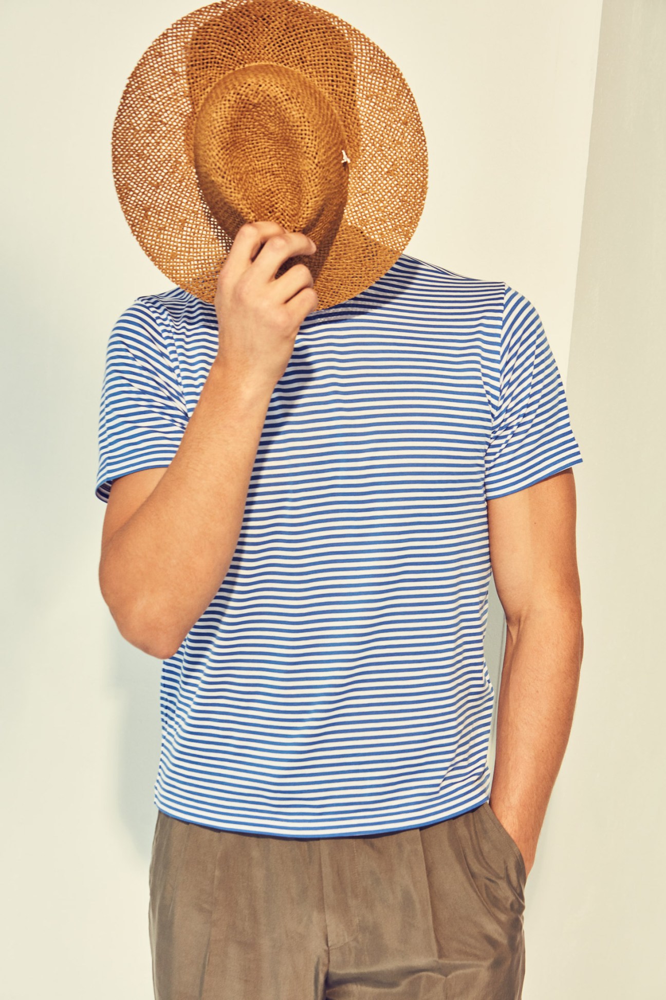 Model wearing blue and white striped t-shirt by Fedeli for Drake's, beige trousers by Ermenegildo Zegna, and woven straw hat by Mühlbauer.