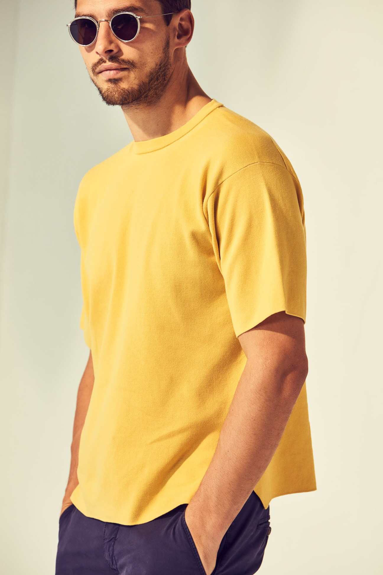 Man wearing a yellow t-shirt by Batoner, navy trousers by Jacob Cohën, and round sunglasses by Eyevan 7285.