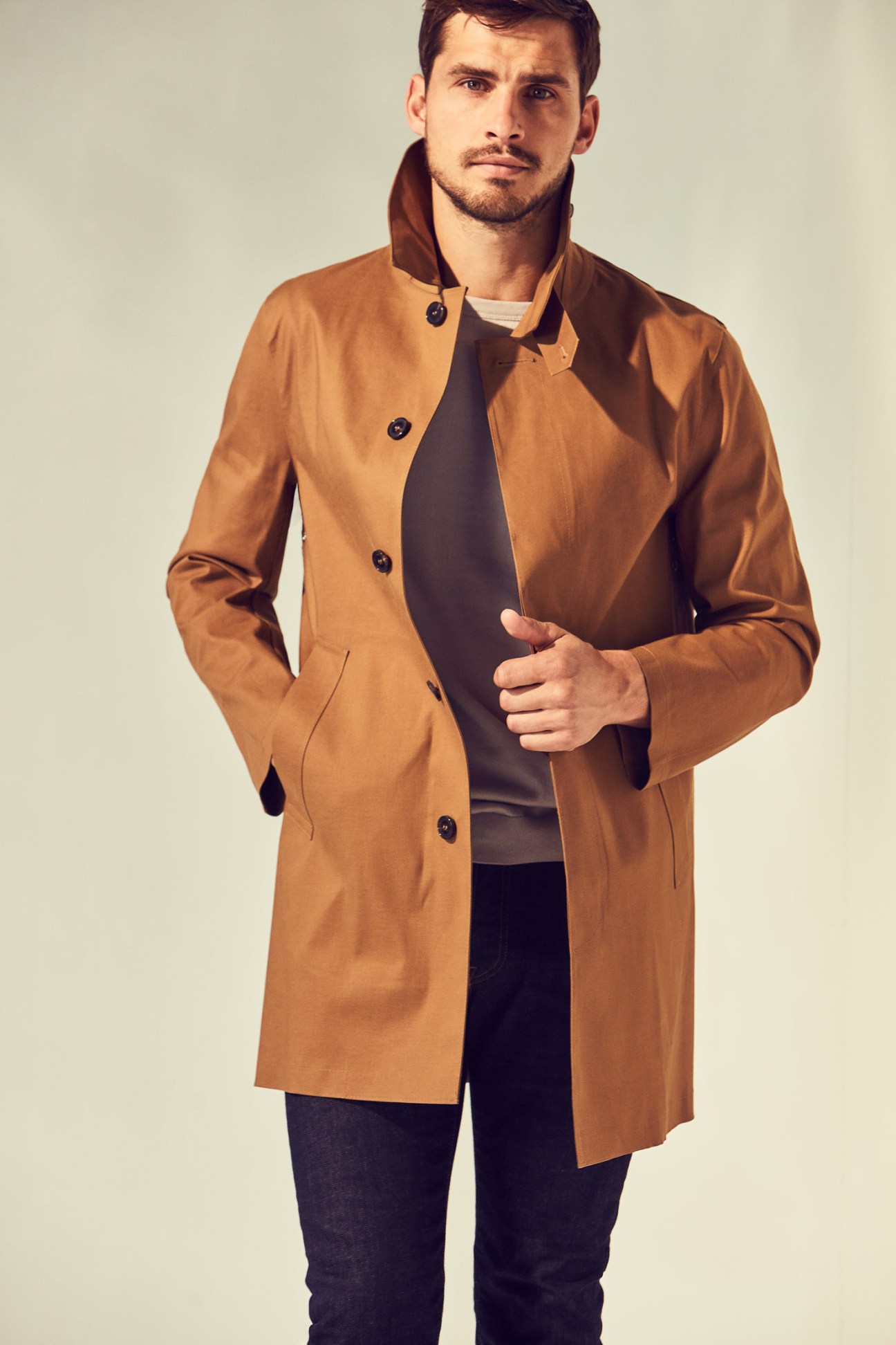 Man wearing a camel-colored coat by Mackintosh over a sleeveless t-shirt and jeans.