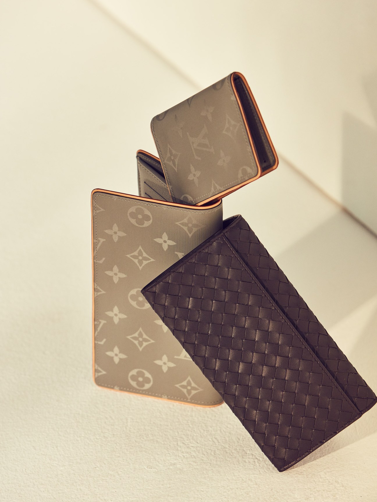 Louis Vuitton wallet and card case with Bottega Veneta wallet arranged on a neutral background.