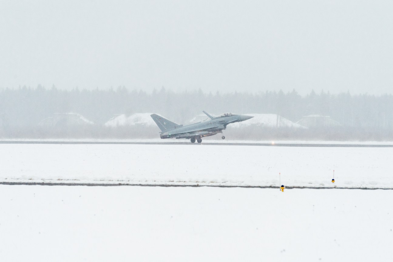 A German Eurofighter jet takes off from a snowy runway in heavy fog and low visibility conditions.