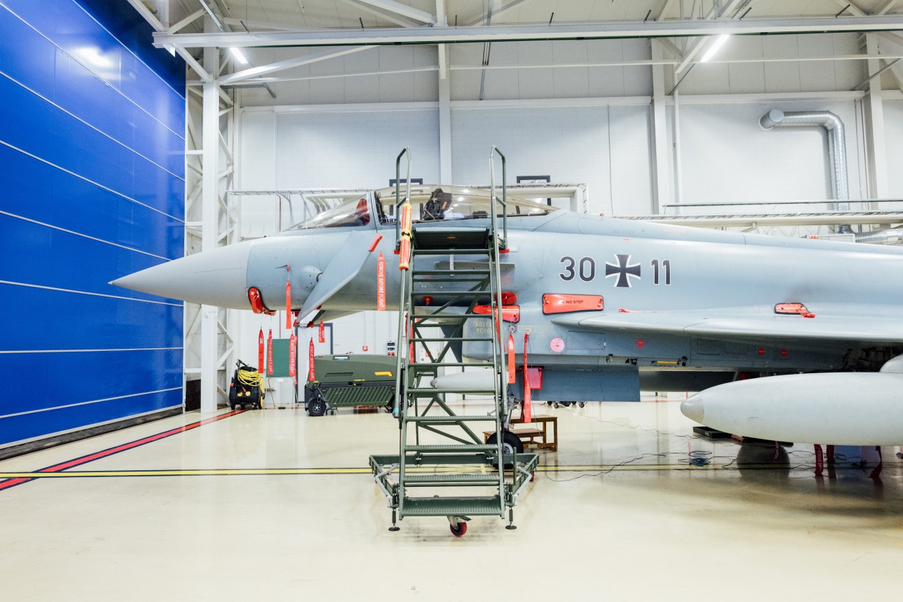 A German Eurofighter jet undergoing maintenance in a hangar with service ladder and equipment nearby.