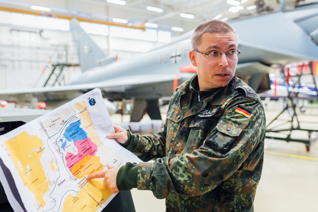 German Luftwaffe officer in camouflage uniform holding a colored map inside an aircraft hangar at Ämari airbase.