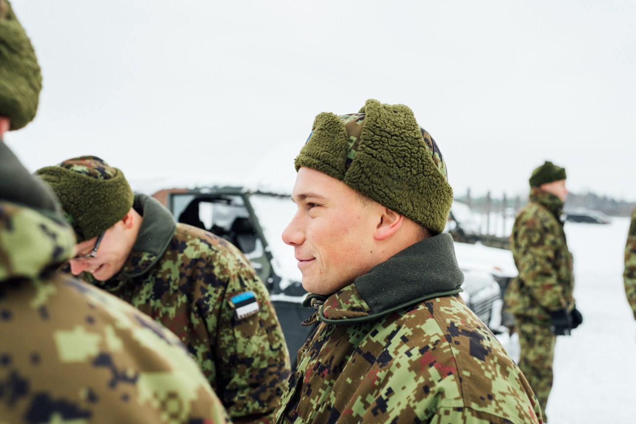 Estonian soldiers in camouflage uniforms and winter gear standing outdoors at a military base.