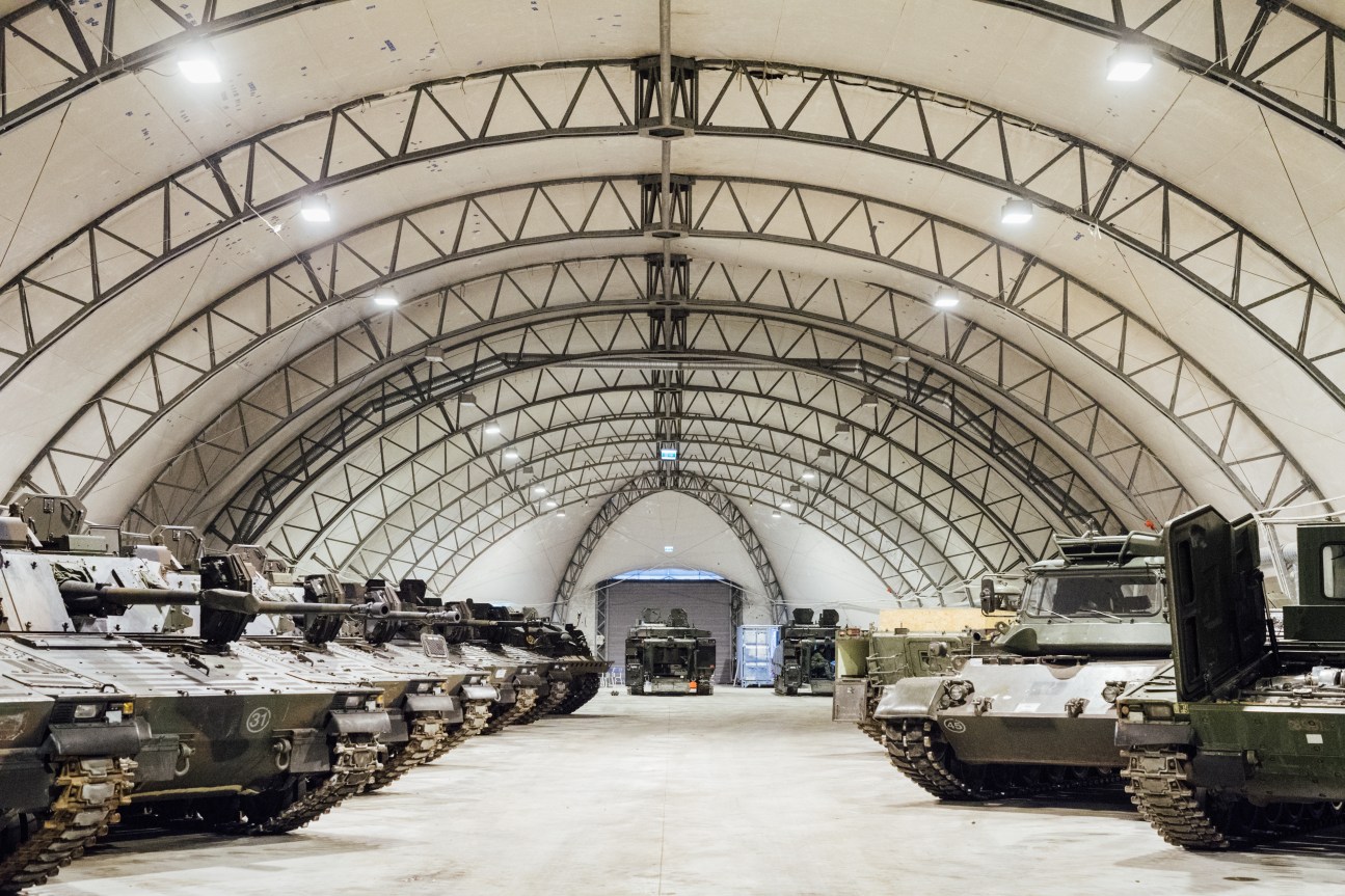 Military tanks lined up inside a large curved-roof hangar at Tapa army base in Estonia.