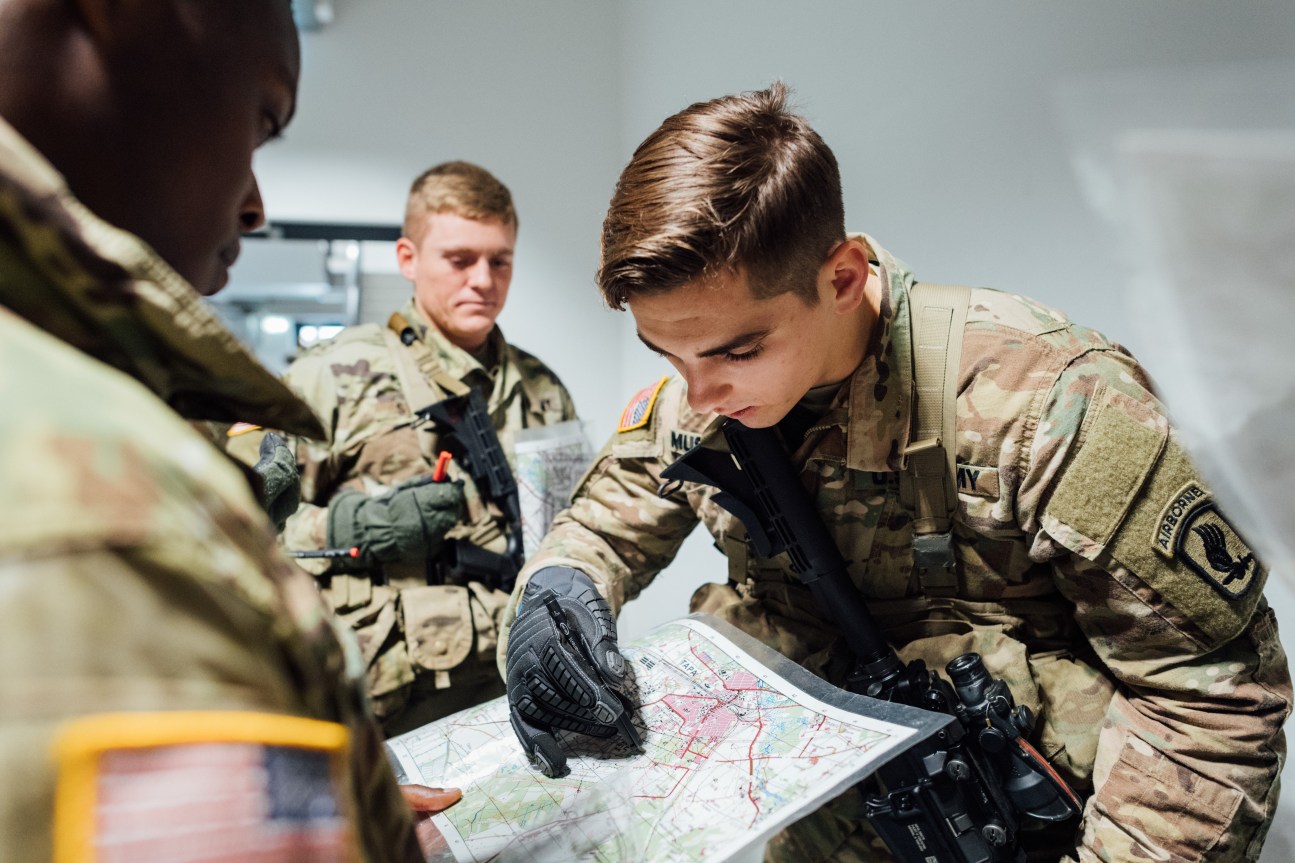 US soldiers in camouflage uniforms study a tactical map together indoors.