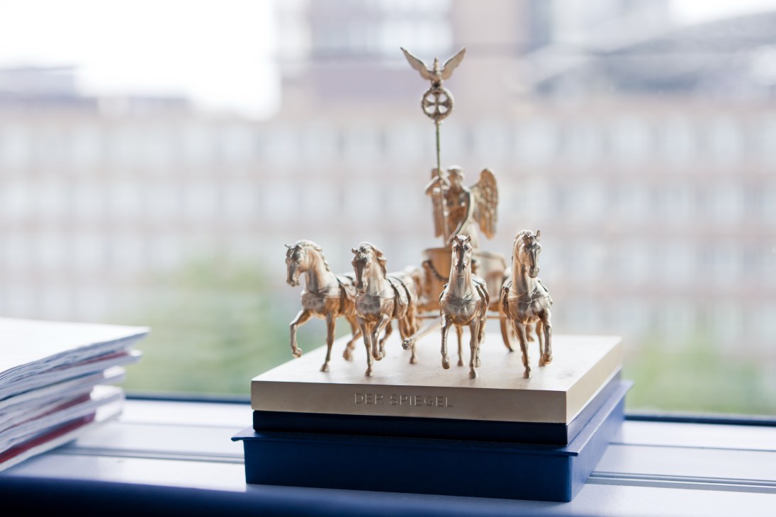 Quadriga of Victory statue on desk with Der Spiegel magazines and blurred Hamburg cityscape in background.