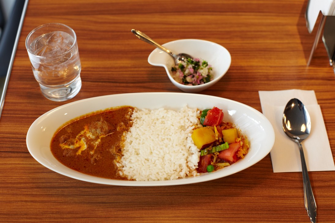 Curry dish with rice and vegetables served on white plate with glass of water on wooden table