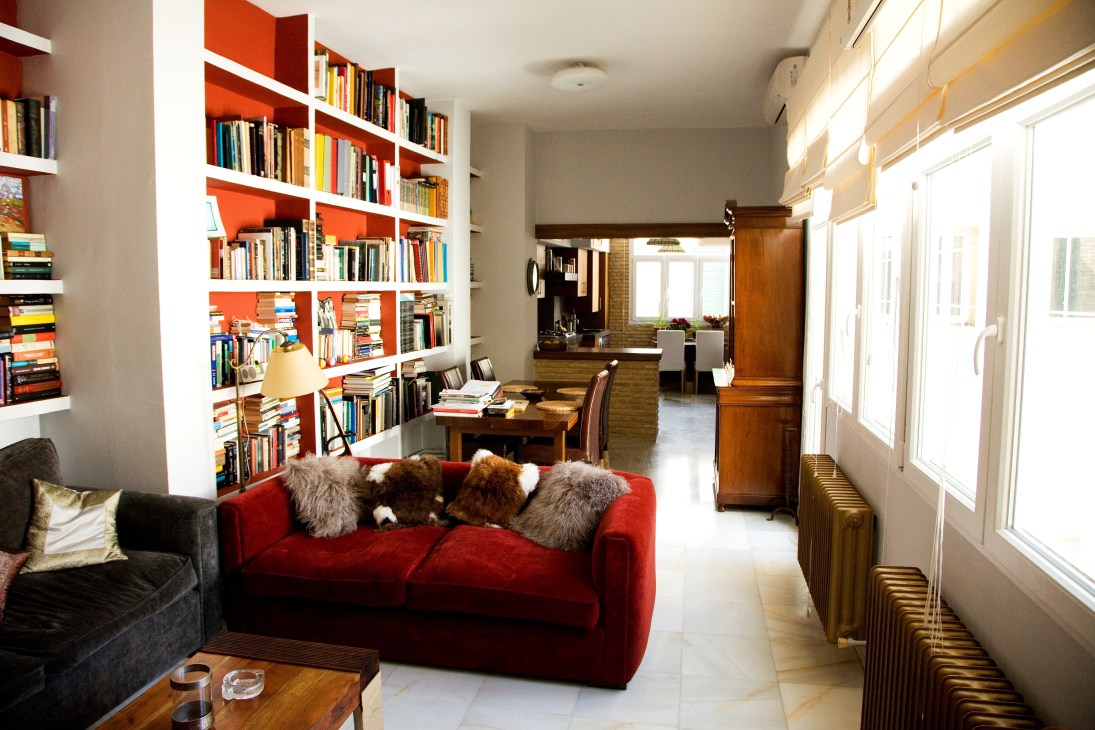 Modern living room with red sofa, orange shelving, wooden desk and bright windows.