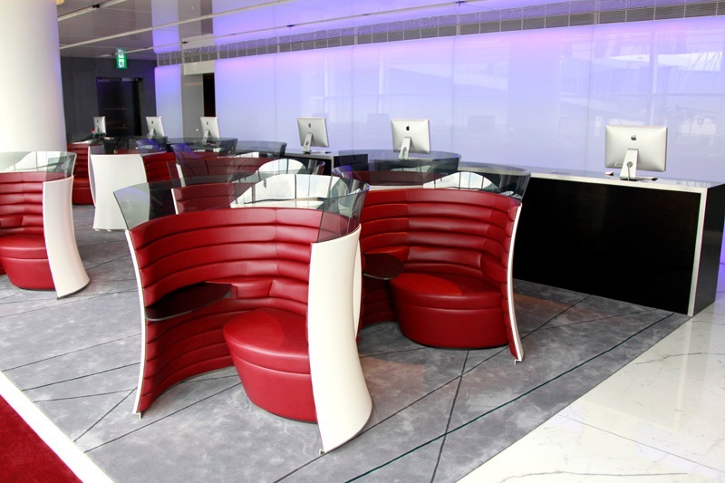 Modern airport lounge with red and white curved seating pods, computer workstations, and purple ambient lighting.