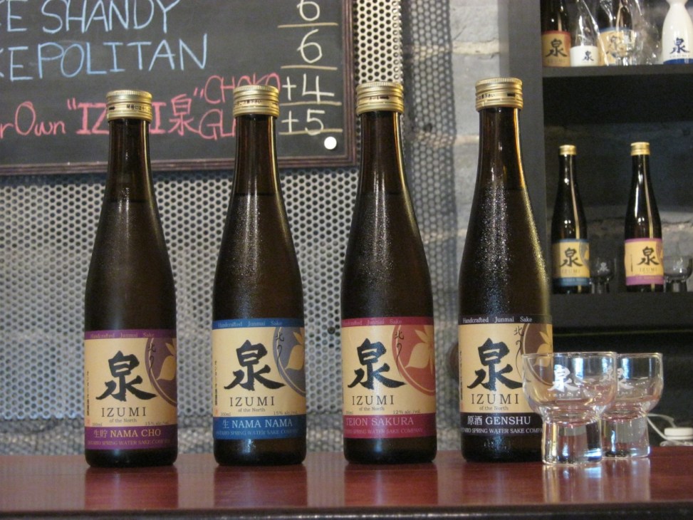Bottles of Izumi sake displayed at Ontario Spring Water Sake Company tasting station with small glasses.