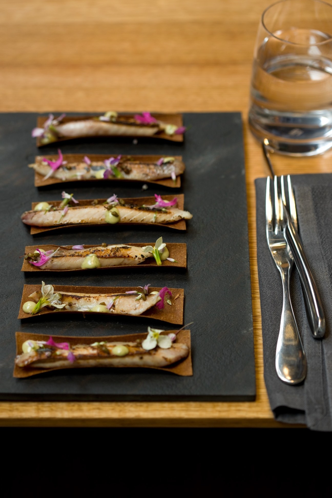 Plated fish dishes with edible flowers on wooden presentation boards at Garagistes restaurant.