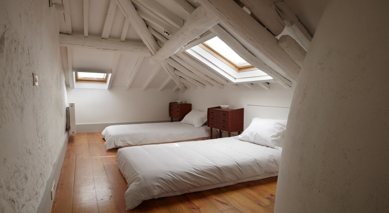 Bright attic bedroom with two beds, wooden floor, white walls and skylight windows at Favorita hotel.