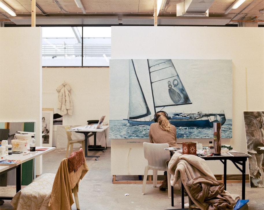 Fine art studio with students working at desks, sailboat artwork on wall, natural light from windows.