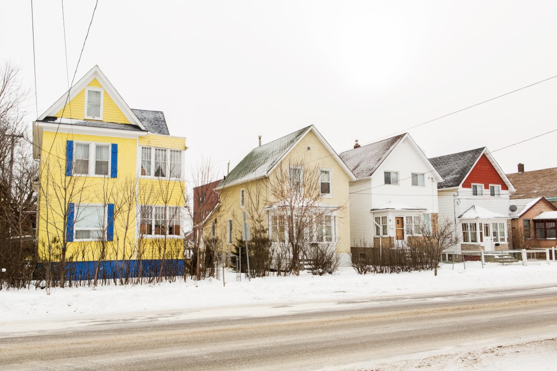 Row of colorful residential houses on a snowy street in Thunder Bay with bare trees and power lines.
