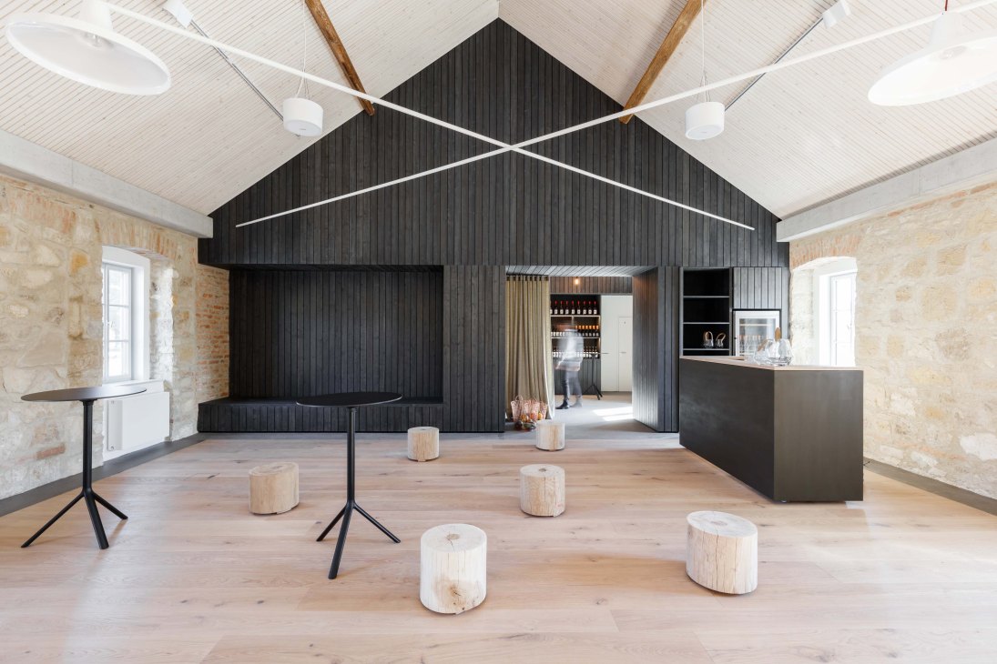 Modern event space inside refitted farmhouse with black interior structure, wooden seating, and stone walls.