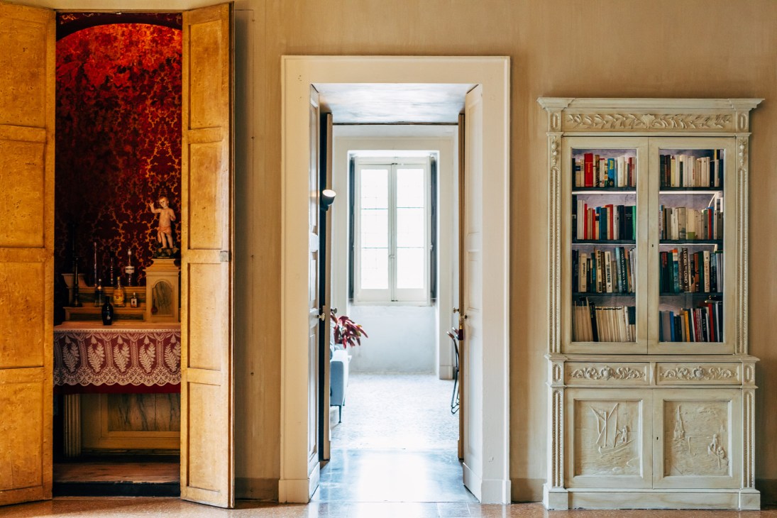 Interior hallway with wooden doors opening to a reading room featuring a cream-colored bookcase with glass doors.