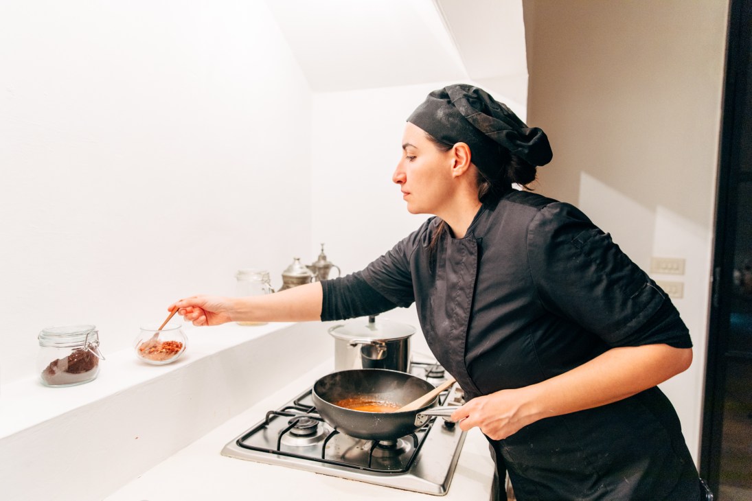 Chef Federica de Giorgi cooking at a stovetop in a minimalist kitchen, adding ingredients to a pan.
