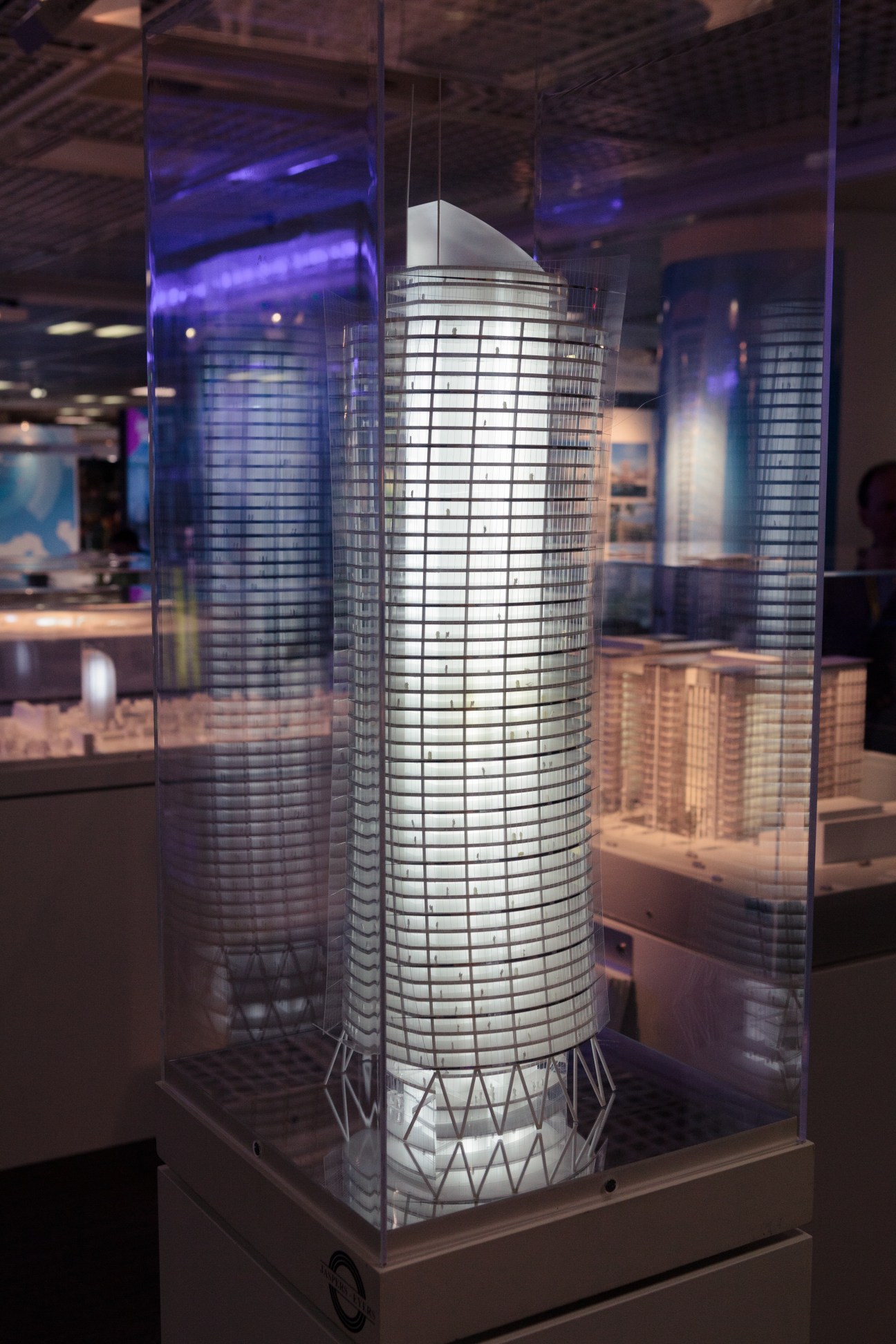 Illuminated architectural model of a tall cylindrical tower displayed in a glass case at Mipim.