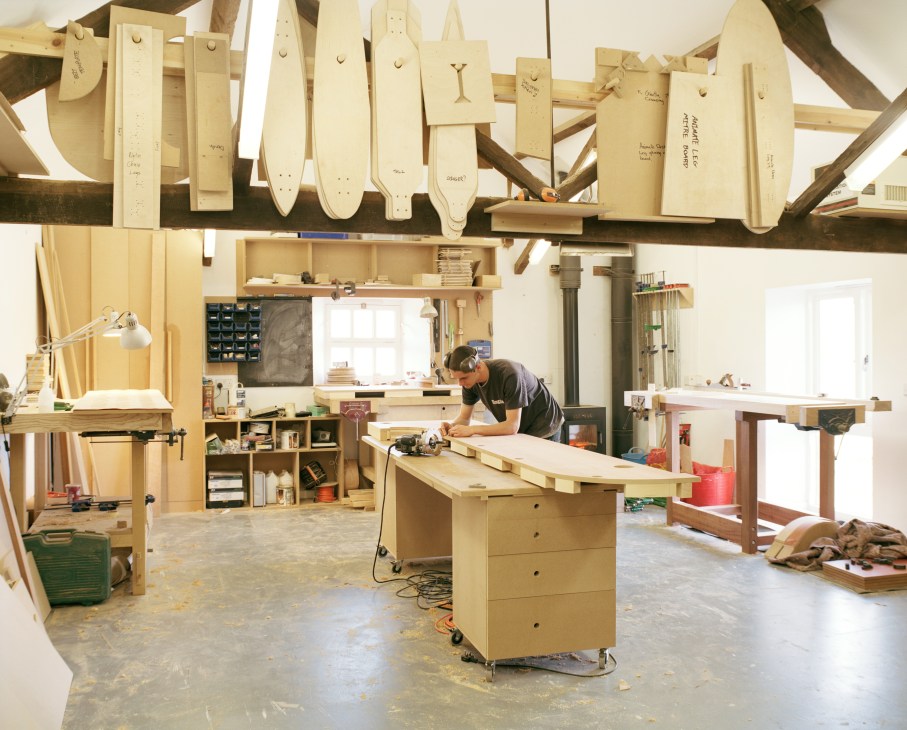 Furniture maker working on wood in Young and Norgate workshop with handcrafted pieces hanging above.