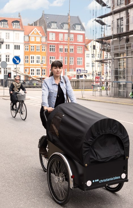 Woman with Christiania cargo bike in Copenhagen square with colorful historic buildings.