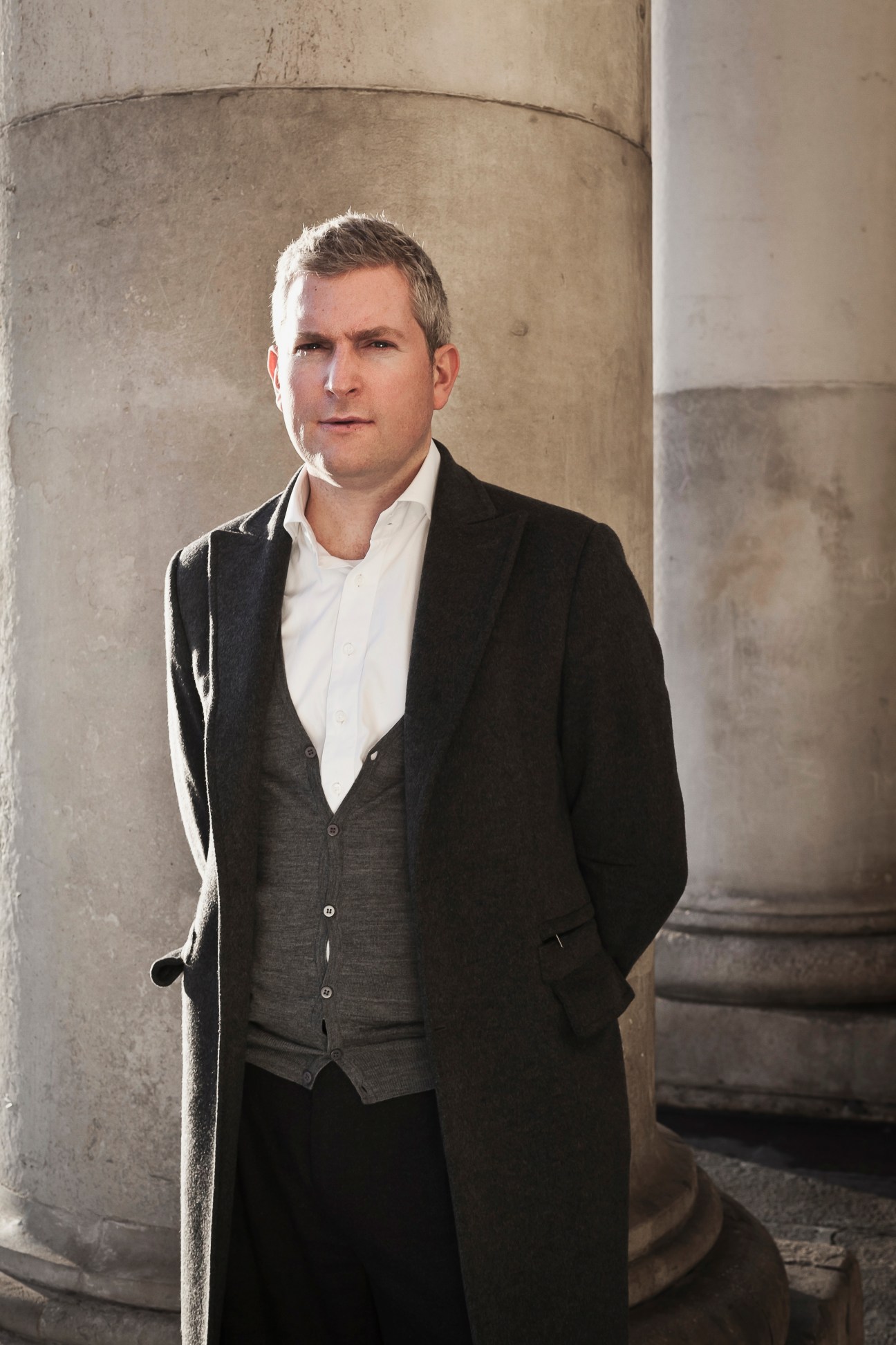 Financier John Bohill of Kish Capital stands in a formal portrait against a concrete pillar.