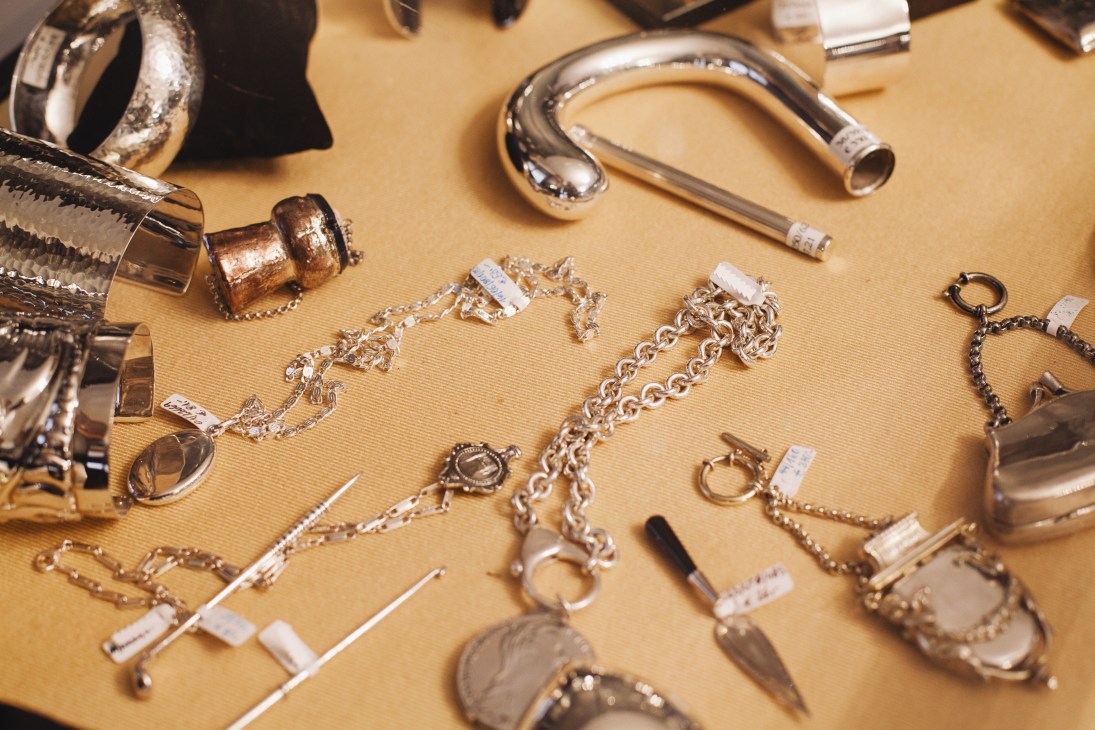 Silver bracelets, chains, and decorative items displayed on a pale yellow surface at Jarosinski & Vaugoin.