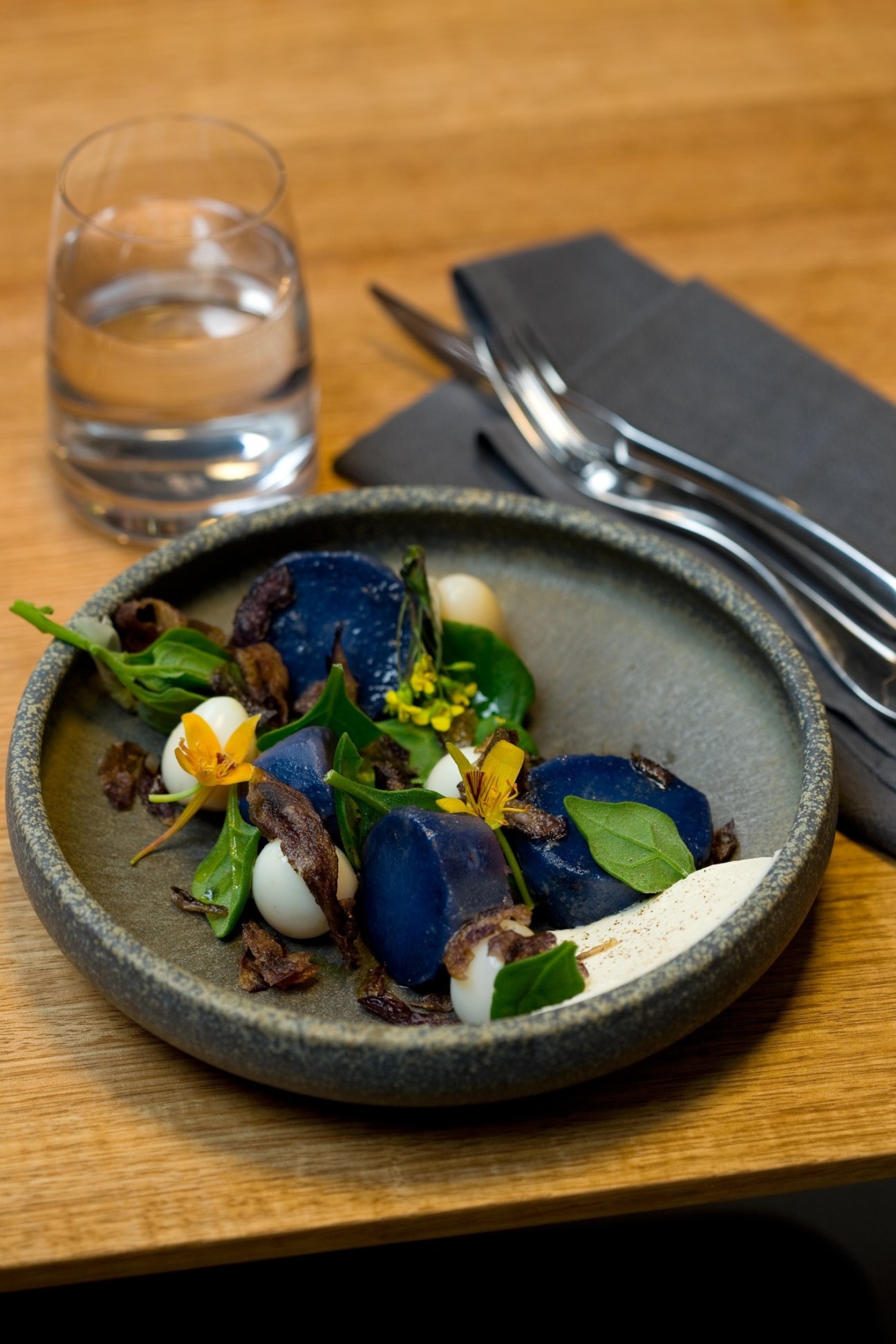 Artfully plated dish at Garagistes featuring dark blue beetroot, white elements, edible flowers and microgreens on gray ceramic plate.